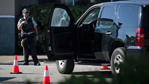 A police officer stands near a vehicle with bullet holes in the windshield and driver's side window at the scene of a shooting in Langley, British Columbia.