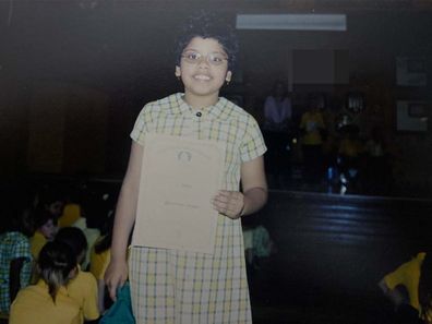 Author standing in the middle of a school assembly in school uniform, holding a certificate.