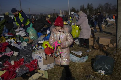 A Ukrainian refugee girl collects a toy from a pile of donated clothes at the Medyka border crossing, in Medyka, Poland, Saturday, Feb. 26, 2022. The U.N. refugee agency said Saturday that nearly 120,000 people have so far fled into neighboring countries and that number is going up fast. (AP Photo/Bernat Armangue)