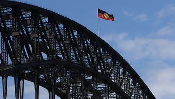 The Australian Aboriginal Flag flies high atop the Sydney Harbour Bridge for the first time since the federal government announced it had paid more than $20 million to Luritja artist Harold Thomas and licence holders to secure copyright for the iconic flag. Pictured on Australia Day 26th January, 2022. Photo: Dylan Coker/The Sydney Morning Herald