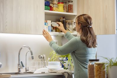 Mature hispanic woman taking out a food can from cupboard kitchen