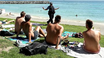 A Western Australia Police officer reminds men at a beach of social distancing requirements.