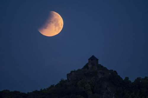 The moon during an eclipse above the Salgo Castle as viewed from Salgotarjan, Hungary, early Monday, May 16, 2022. (Peter Komka/MTI via AP)