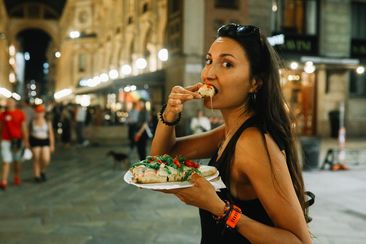 Woman having a pizza slice on the go on the streets of Milano, Italy, in the evening.