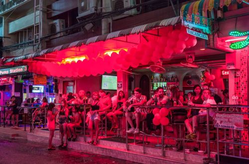 The neon-lit bar on a busy street sees locals mingling and sharing drinks with tourists.
