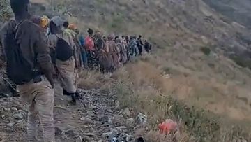 A video shows a group of migrants walking along a steep slope inside Saudia Arabia on the trail used to cross from the migrant camp of Al Thabit
