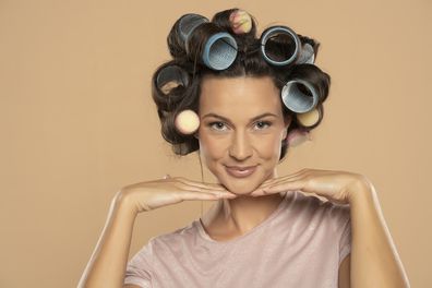 Beautiful smiling woman with hair curlers posing on a beige studio  background