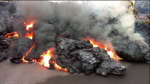 In this photo from video a lava flow advancing down a road is seen from less than 10 feet away in the Leilani Estates subdivision near Pahoa on the island of Hawaii Monday, May 7, 2018. Kilauea volcano has destroyed more than two dozen homes since it began spewing lava hundreds of feet into the air last week, and residents who evacuated don't know how long they might be displaced. The decimated homes were in the Leilani Estates subdivision, where molten rock, toxic gas and steam have been bursting through openings in the ground created by the volcano. (Scott Wiggers/Apau Hawaii Tours via AP)
