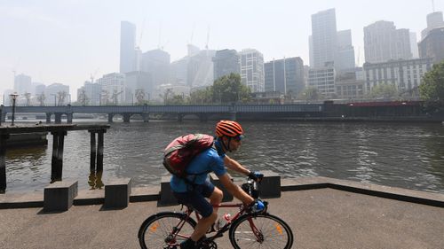 A cyclist rides along the Yarra River in Melbourne, Friday, January 3, 2020. A smoke haze has drifted over the city from the bushfires in East Gippsland