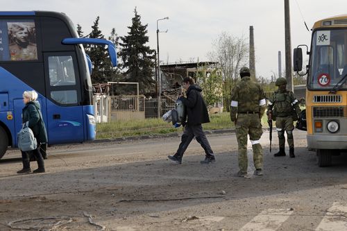 Local residents who left a shelter in the Metallurgical Combine Azovstal walks to a bus escorted by servicemen of Russian Army and Donetsk People's Republic militia in Mariupol, in territory under the government of the Donetsk People's Republic, eastern Ukraine, Friday, May 6, 2022. (AP Photo/Alexei Alexandrov)