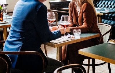 A couple holding hands while sitting down at a table and drinking red wine in a restaurant for lunch together.