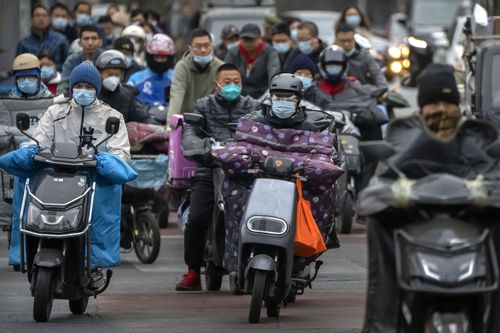 Des navetteurs portant des masques faciaux conduisent des scooters dans une rue du quartier central des affaires de Pékin, le vendredi 28 octobre 2022 