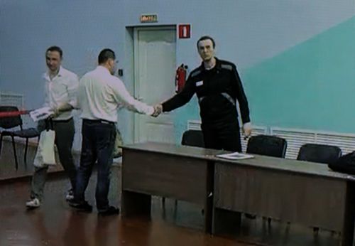 Russian opposition politician Alexei Navalny appears on a screen via video link as he shakes hands with his lawyer Vadim Kobzev before an external hearing of the Moscow City Court in the criminal case against Navalny on numerous charges, including the creation of an extremist organization, at the IK-6 penal colony in Melekhovo in the Vladimir region, Russia, August 4, 2023. 