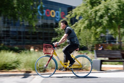 A tech worker rides a bike past signage on the Google campus