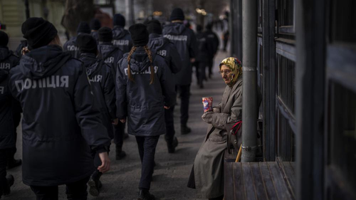 Ukrainian police officers march past a woman begging for alms during a demonstration in Odessa, Ukraine. 