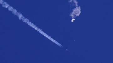 In this photo provided by Chad Fish, the remnants of a large balloon drift above the Atlantic Ocean, just off the coast of South Carolina, with a fighter jet and its contrail seen below it.