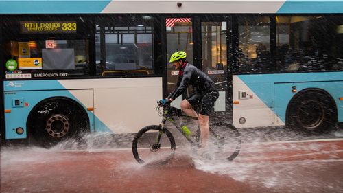 A cyclist is sprayed with water by a bus in Paddington, Sydney.