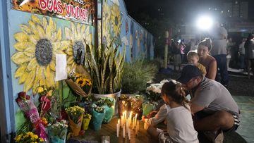 A family lights a candle at a makeshift memorial at the &quot;Cantinho do Bom Pastor&quot; daycare center after a fatal attack on children in Blumenau, Brazil, 