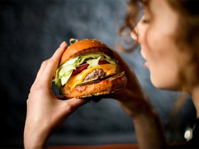 Young woman lifting a cheeseburger to her mouth