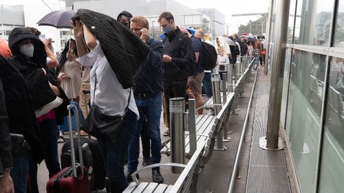 Les gens font la queue devant l'aéroport de Sydney sous la pluie.
