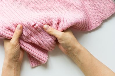 Woman hands holding the knitted thing with hole made by moth