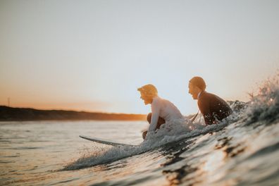 Australian bride and groom surf together before beach wedding