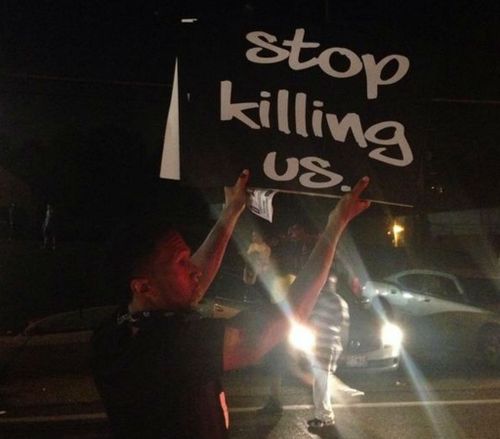 A teenager holds up a sign while protesting in front of a police barricade in Ferguson. (Source: Deray Mckesson, Twitter)