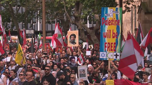Uma multidão de manifestantes pró-palestinos em Sydney segurando cartazes e bandeiras.