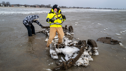 O vereador do Luna Pier, Neil Wakeman, segura um volante enquanto ele e seus amigos olham para um carro que normalmente fica submerso em cerca de 2,5 metros de água, a cerca de 100 metros da praia em Luna Pier, Michigan, segunda-feira, 29 de dezembro de 2025. (Andy Morrison/Detroit News via AP)