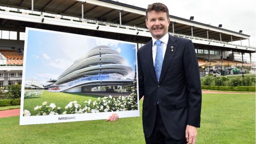 VRC Chairman Michael Burn poses for a photo with an artist impression of the proposed members grandstand front of the 93-year-old existing structure. (AAP)