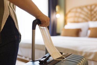 Woman with face mask and suitcase in the hotel room, close up.