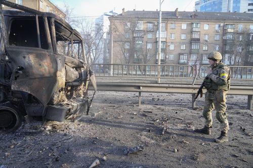 A Ukrainian soldier walks past debris of a burning military truck, on a street in Kyiv, Ukraine, Saturday, Feb. 26, 2022. Russian troops stormed toward Ukraine's capital Saturday, and street fighting broke out as city officials urged residents to take shelter. (AP Photo/Efrem Lukatsky)