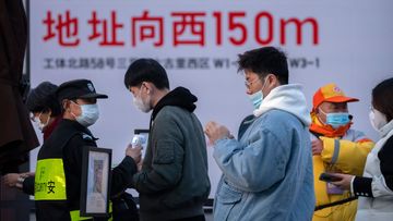 People wearing face masks to protect against COVID-19 have their temperature and health codes checked by a security guard as they enter an outdoor shopping center in Beijing.