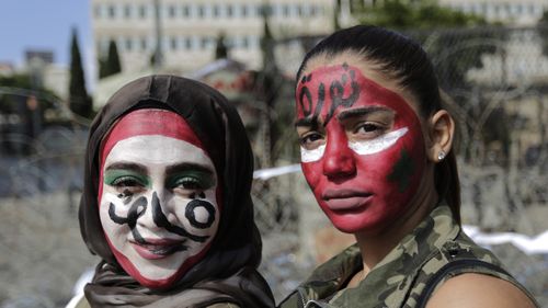 Anti-government protesters with the colors of the Lebanese national flag painted on their faces and with Arabic that reads "Revolution," pose for a photograph in front of the government palace in Beirut.