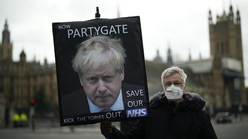 Protestujący antykonserwatywny trzyma transparent z wizerunkiem premiera Wielkiej Brytanii Borisa Johnsona z wypisanymi słowami "Teraz impreza" Na tle Houses of Parliament w Londynie. 