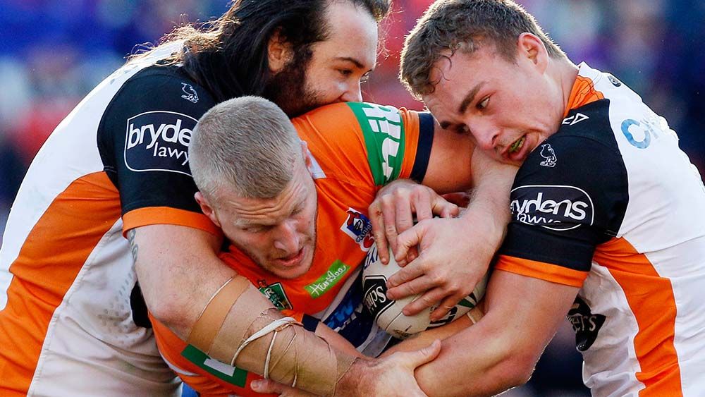 Mitchell Barnett of the Knights is tackled by Aaron Woods and Jacob Liddle of the Tigers