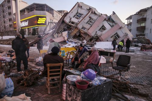 People sit and stand around a collapsed buildings in Golbasi, in Adiyaman province, southern Turkey, Wednesday, Feb. 8, 2023. 