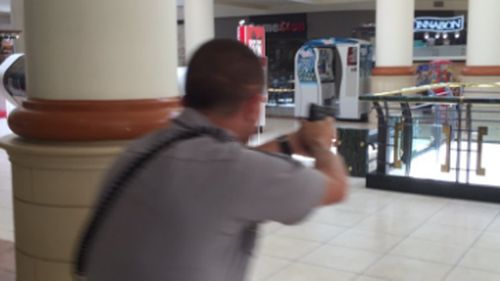 A police officer draws his gun inside the shopping centre. (Twitter: Tony Rice)