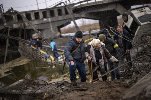 Des miliciens locaux aident une vieille femme à traverser un pont détruit par l'artillerie, alors qu'elle tente de fuir, à la périphérie de Kiev, en Ukraine, mercredi 2 mars 2022.