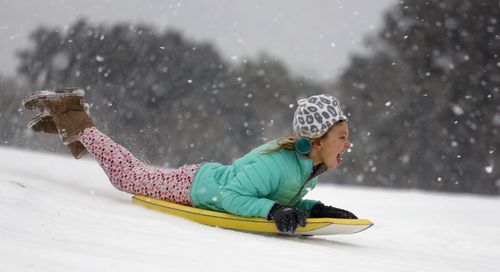 A Carolinas native uses a beach boogie board as an improvised snow sled. (Image: AAP)