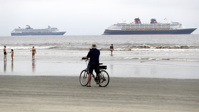 The Disney Wonder cruise ship, right, sits at anchor in front of Celebrity Cruise's Millennium cruise ship, as people pass on the beach Thursday, April 30, 2020, in Coronado, Calif. 