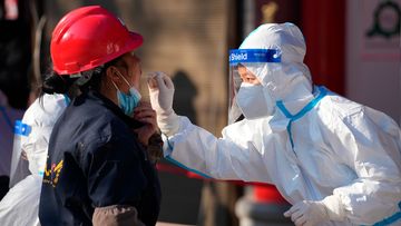 A worker wearing a protective suit collects a throat swab sample at a COVID-19 testing site in Xi&#x27;an.
