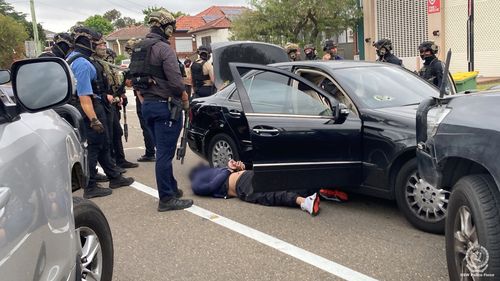 Multiple heavily armed police officers surround a vehicle and a man they arrested in Sydney's south-west.