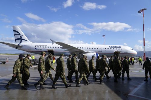 Greek soldiers pass in front of an aircraft, loaded with humanitarian aid at Eleftherios Venizelos International Airport in Athens, on Sunday, Feb. 27, 2022