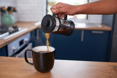 A close up of hand pouring fresh filter coffee into a mug in a clean kitchen
