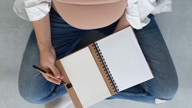 Top view of a pregnant woman sitting cross-legged with a notebook on her lap.