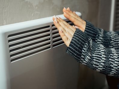 Woman holding hands to heater winter bills energy prices living in poverty cold weather
