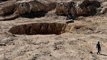 A member of the Hashed al-Shaabi (Popular Mobilisation) paramilitaries walks next to a sinkhole in the village of Athbah, south of Mosul. (AFP)