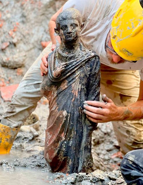 An archaeologists works at the site where two dozen well-preserved bronze statues were found