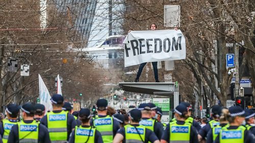 A man holds a banner reading "Freedom" atop a tram stop during an anti-lockdown protest in Melbourne on August 21, 2021. coronavirus 